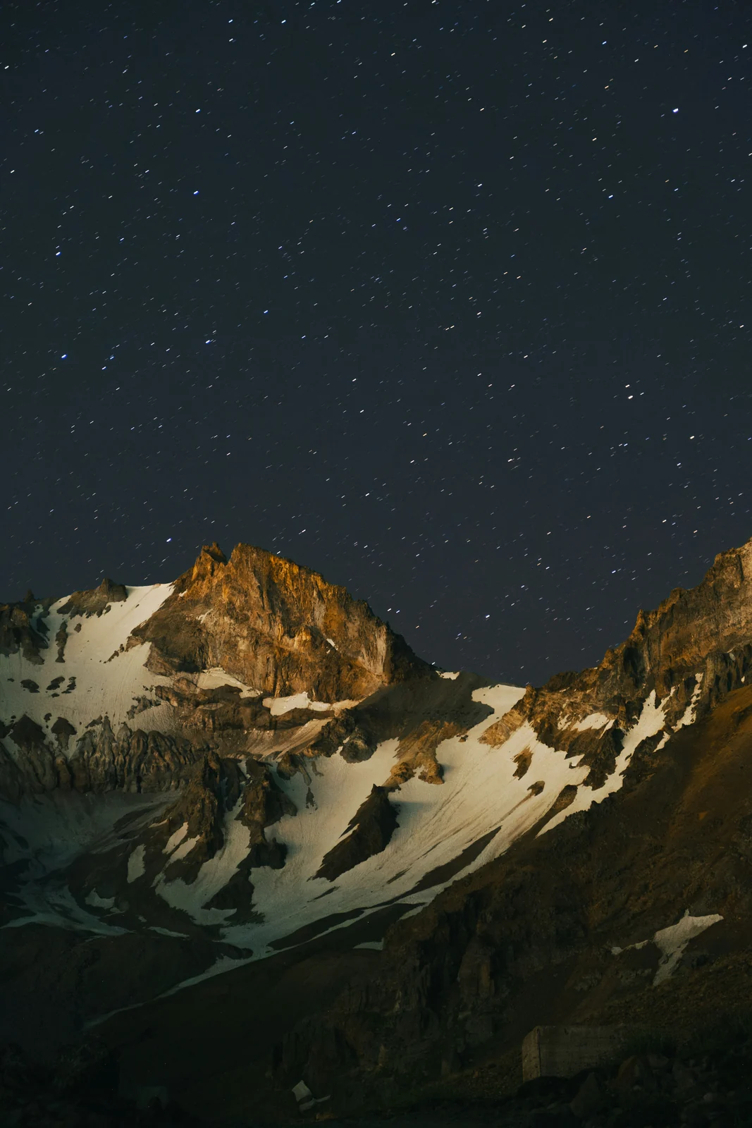 A snow covered mountain peak lit by moonlight beneath a dense field of stars